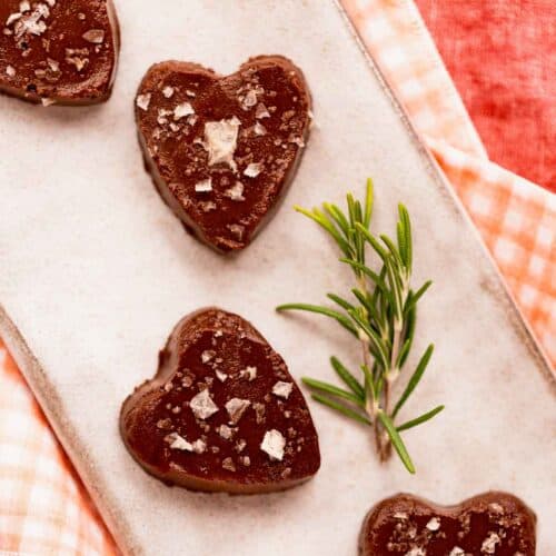 Homemade vegan chocolate rosemary pine nut truffles topped with flake salt next to a fresh rosemary sprig.