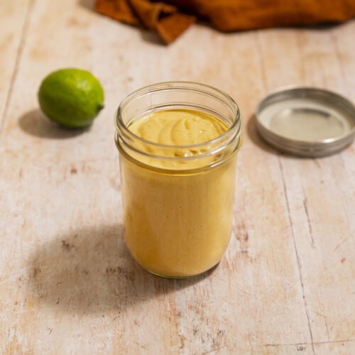 A jar of creamy lime chipotle sauce on a wood surface.