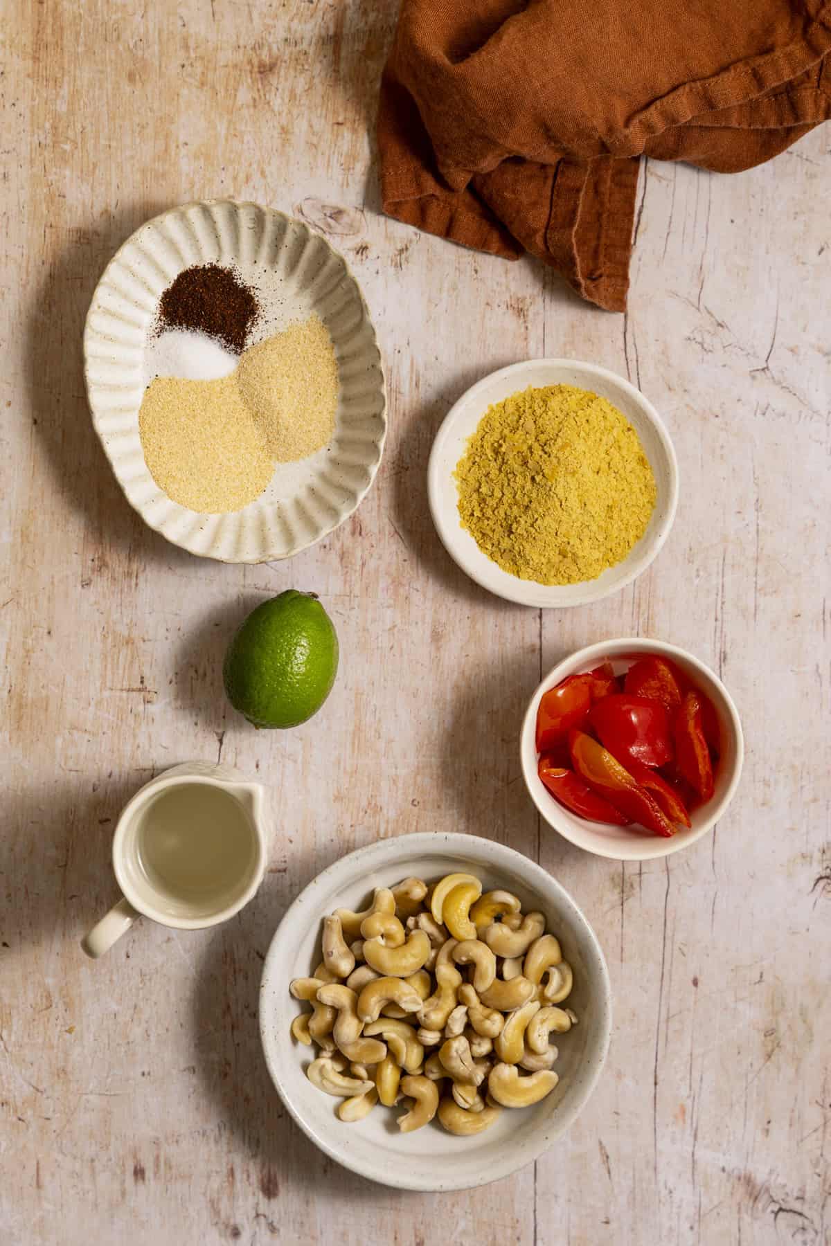 Cashews, bell pepper, and a lime plus spices and water on a wood surface.