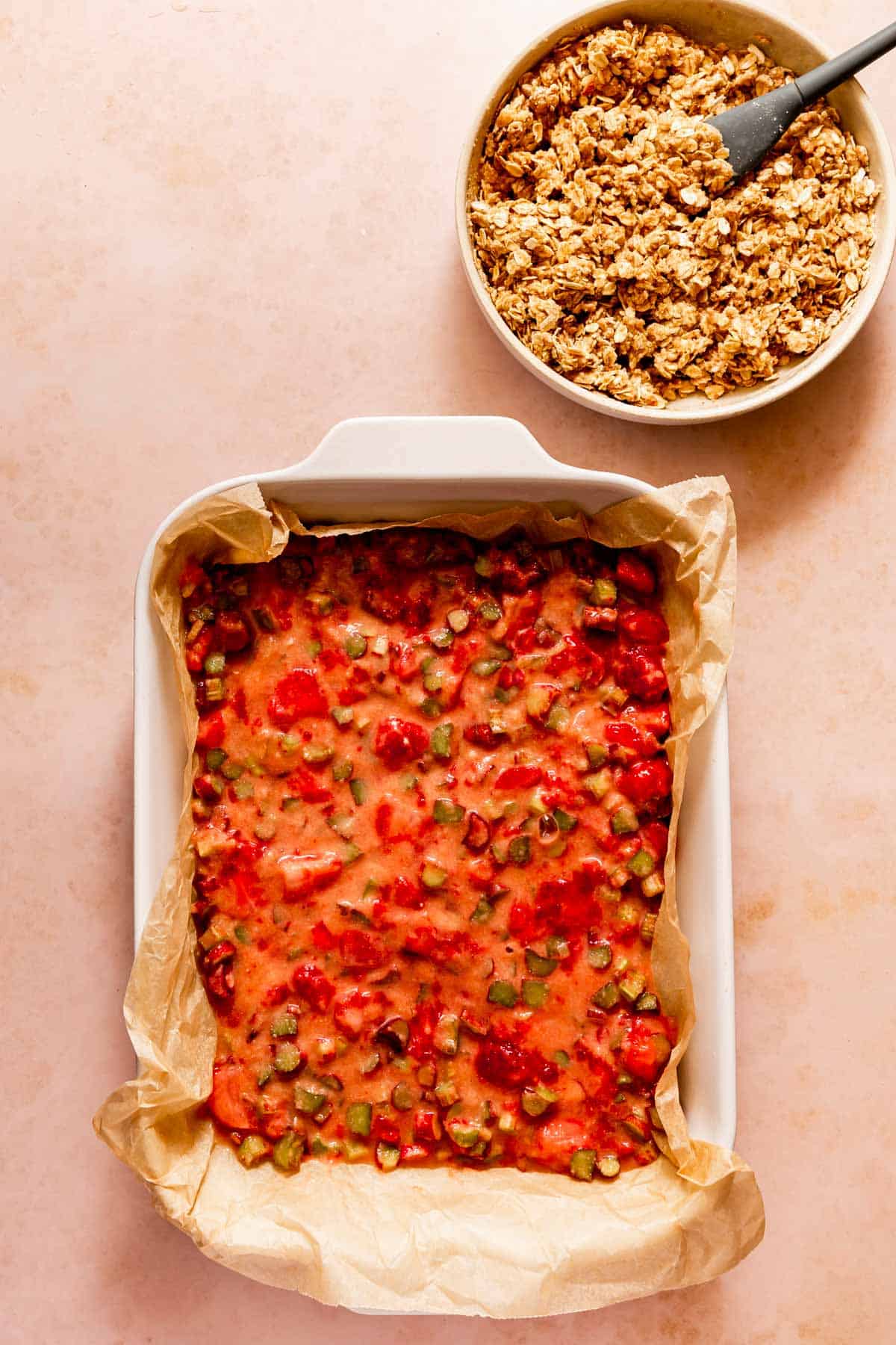 Strawberry and rhubarb in a 9x13 with topping in a bowl above it.