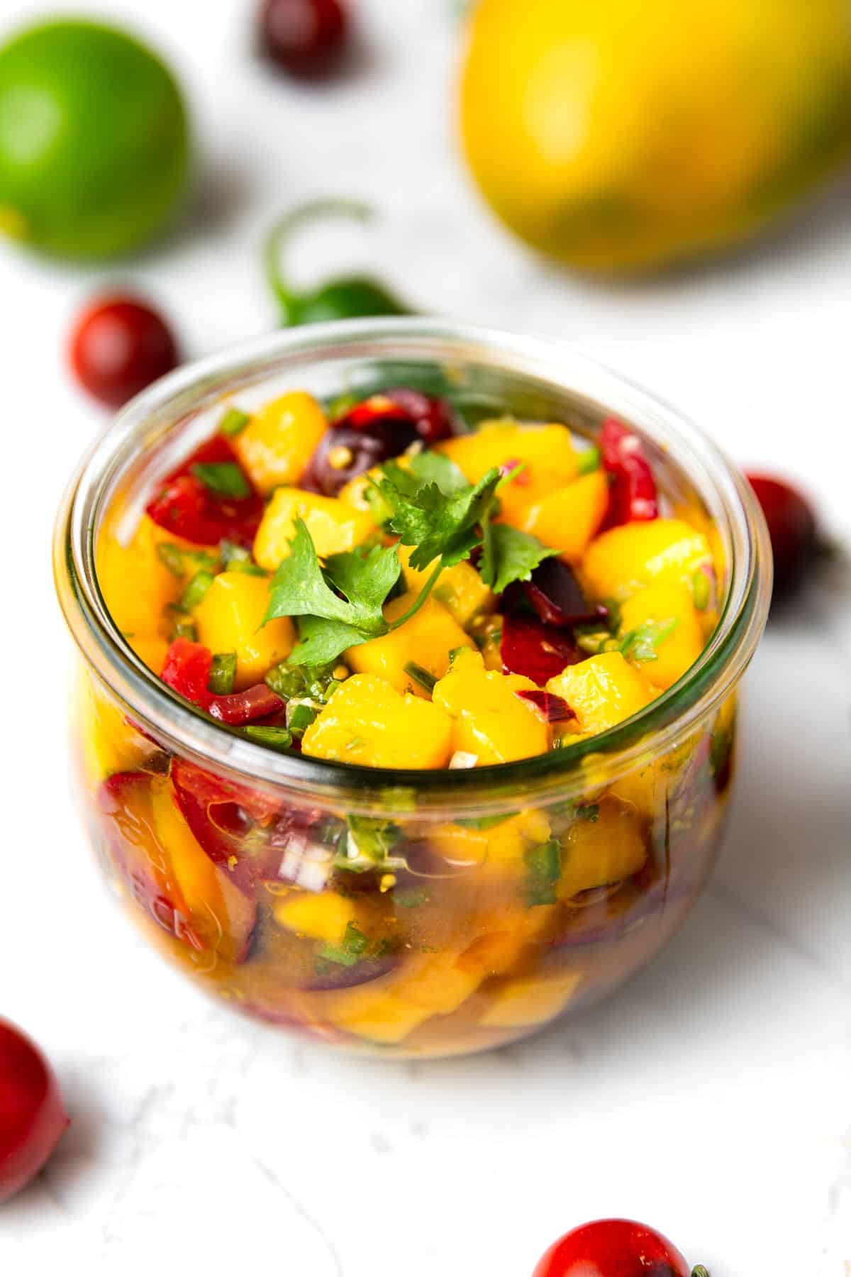 A round glass jar of fresh, chunky mango salsa.