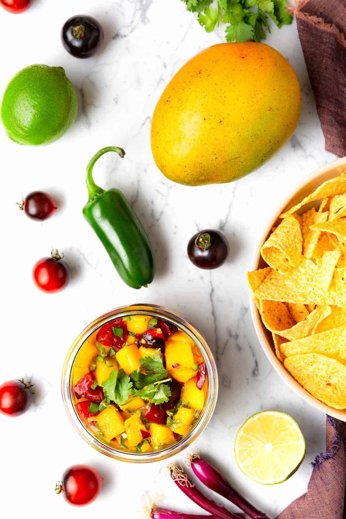 An overhead view of mango salsa surrounded by the five ingredients used to create it and a bowl of tortilla chips.