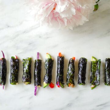 Tiny nori-wrapped veggies laying in a row on a marble surface.