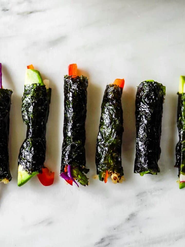A row of little nori-wrapped rolls with veggies poking out on either end, all on a marble surface.