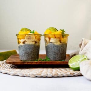 Two chia puddings on a wood tray topped with tropical ingredients