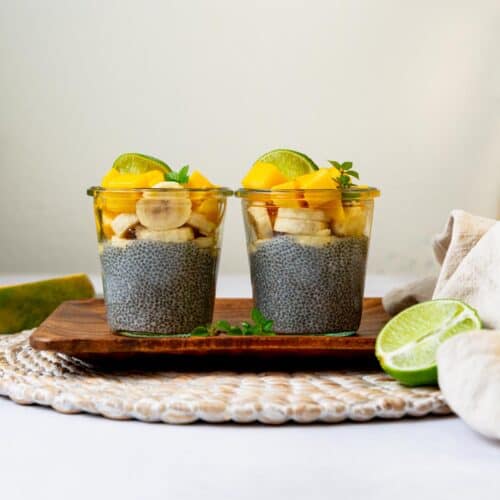 Two chia puddings on a wood tray topped with tropical ingredients