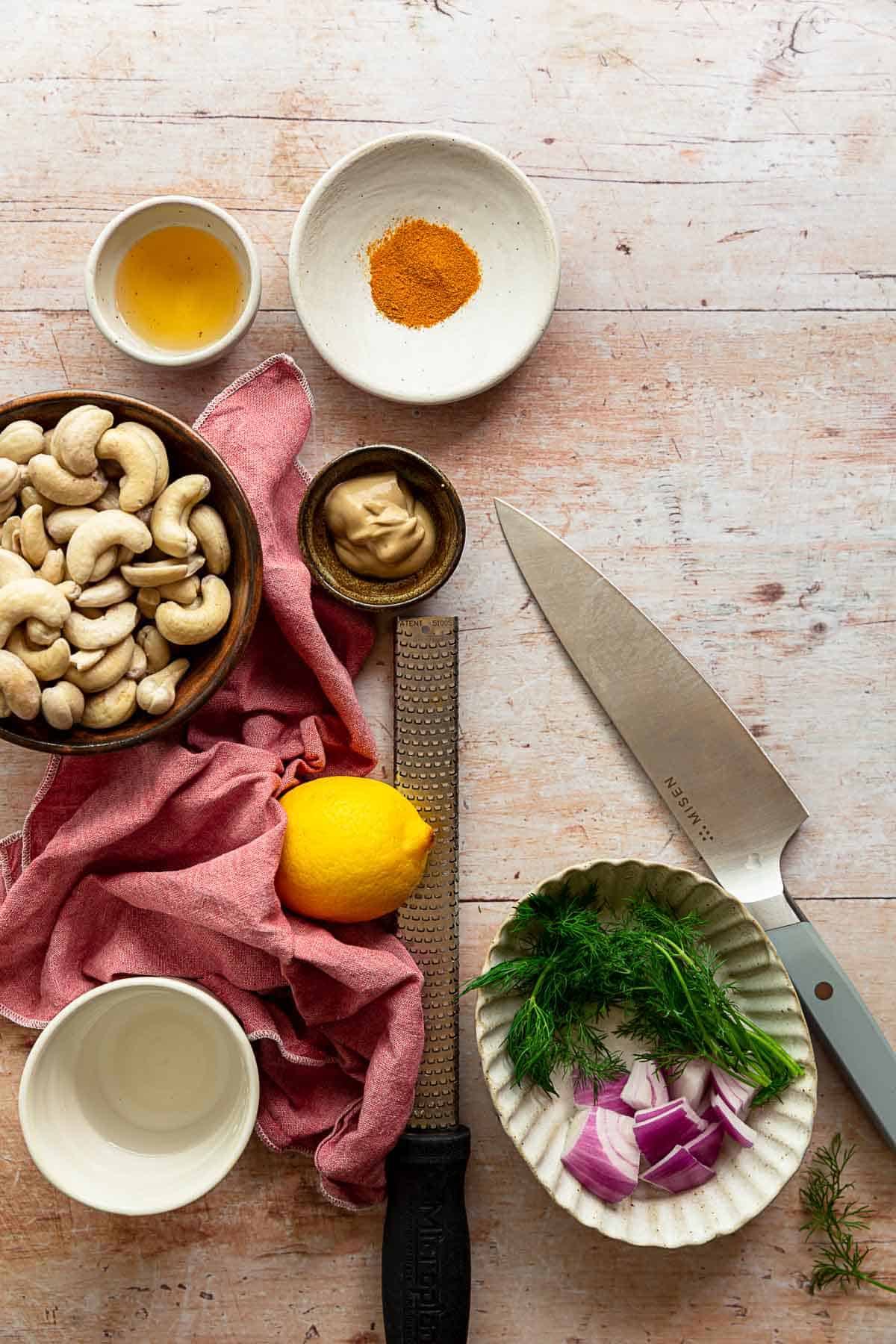 Potato salad dressing ingredients in small bowls on a distressed-wood background with a pink linen.