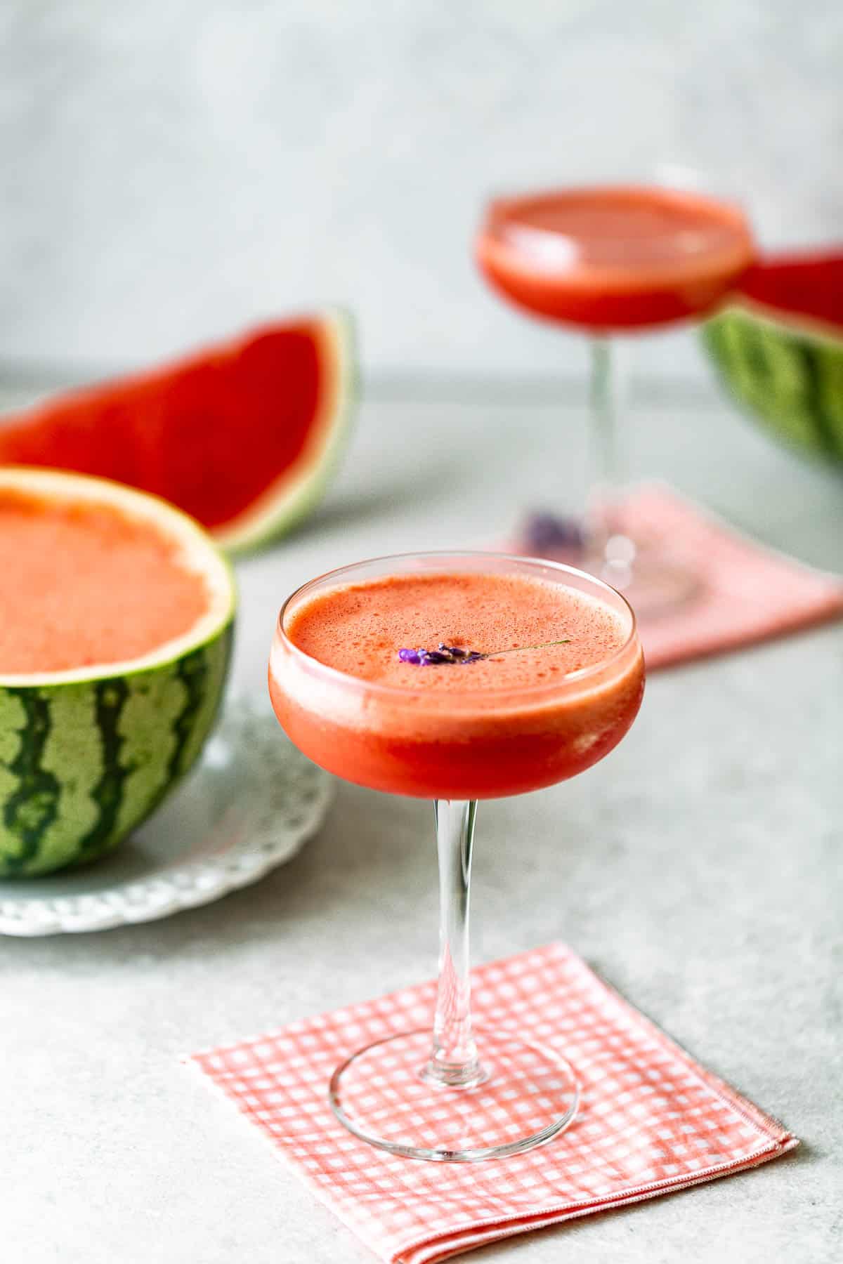 Watermelon lavender daiquiris on a concrete surface surrounded by watermelon and topped with lavender.