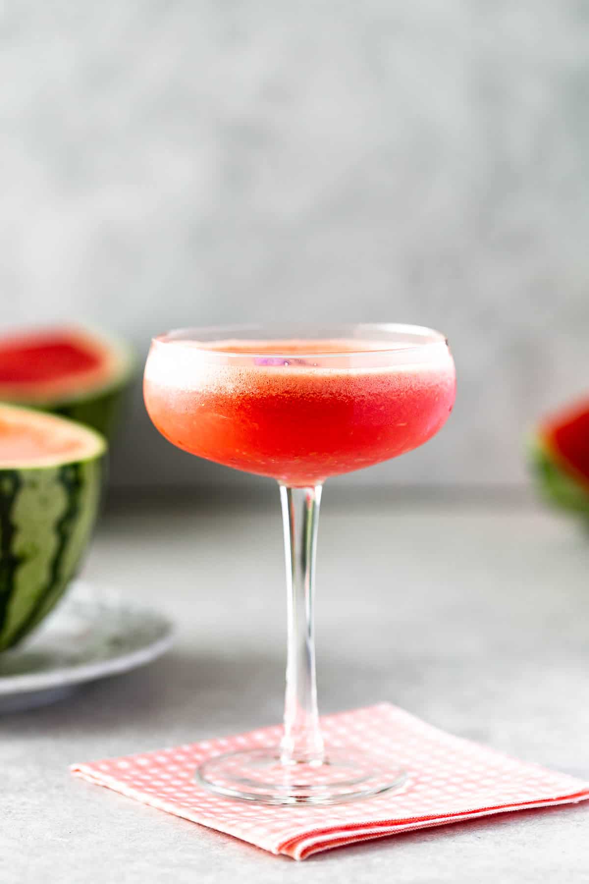 A red cocktail on a pink napkin in front of a halved watermelon.