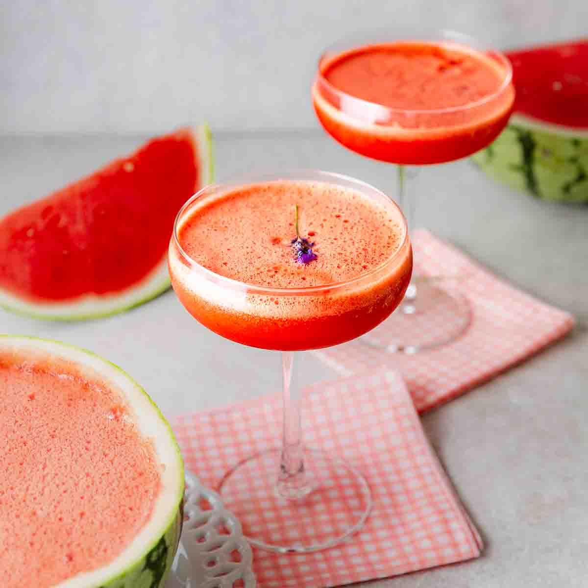 Two glasses of watermelon lavender cocktails topped with a sprig of lavender and surrounded by watermelon.