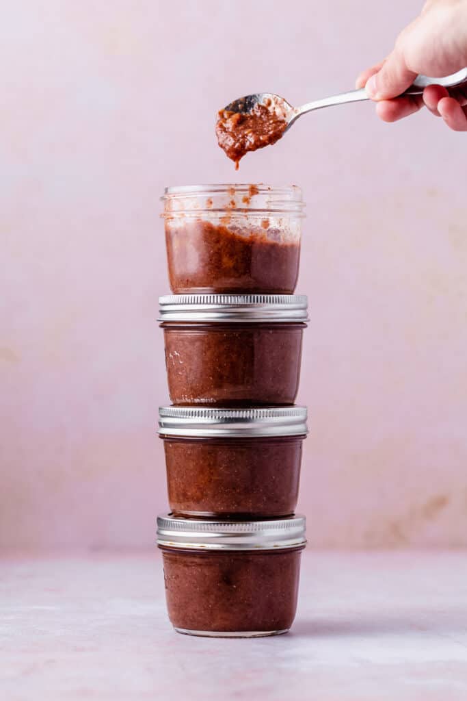 4 plum jam jars stacked on top of each other, the top open with a spoonful of jam above