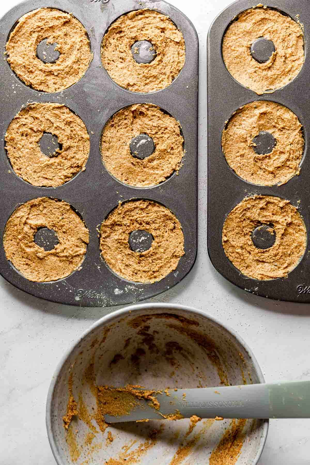 Gluten-free, vegan, oil-free pumpkin donut raw dough in donut pans with an empty mixing bowl below.