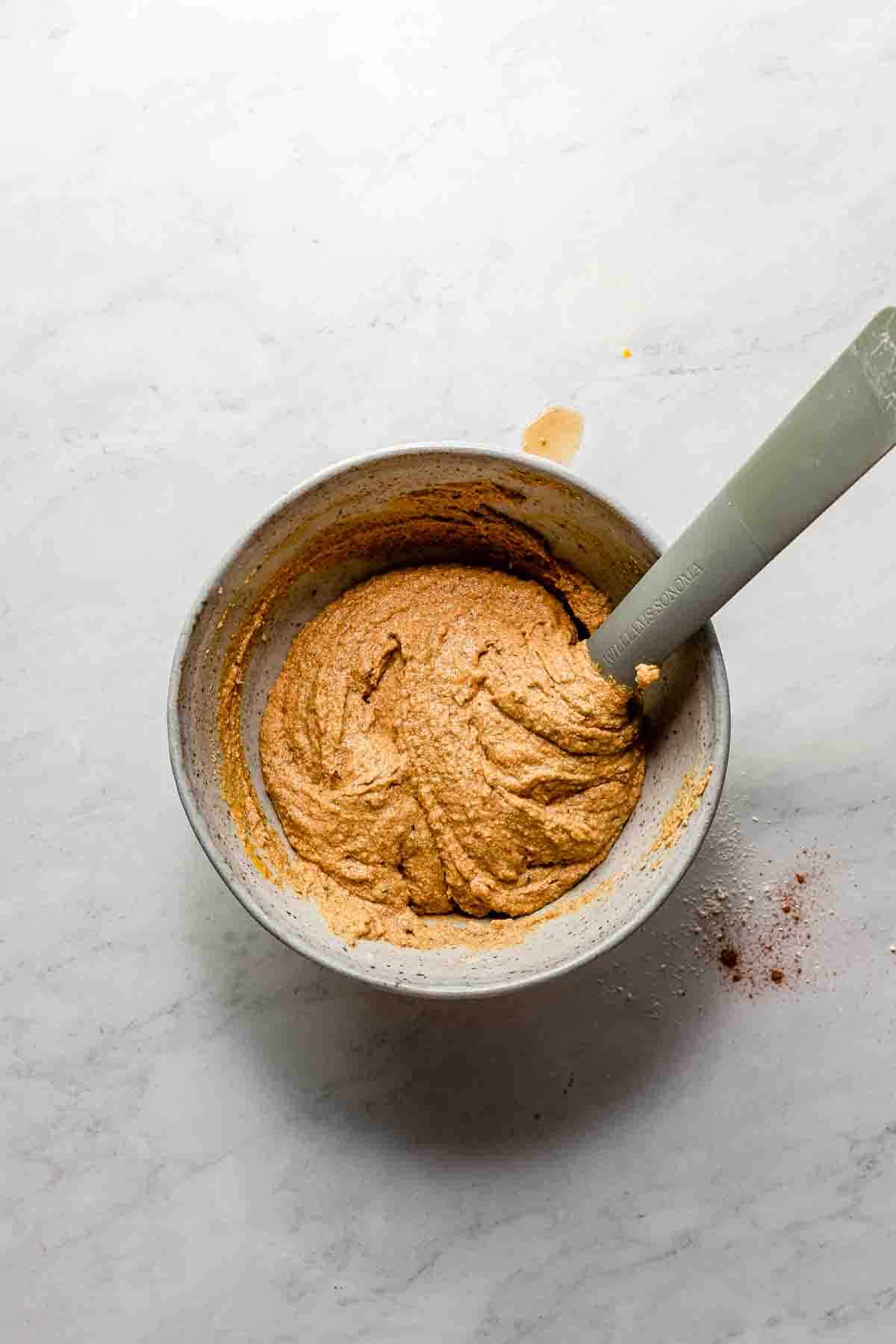 One bowl gluten-free, vegan, oil-free pumpkin donut ingredients being stirred together on a marble surface.