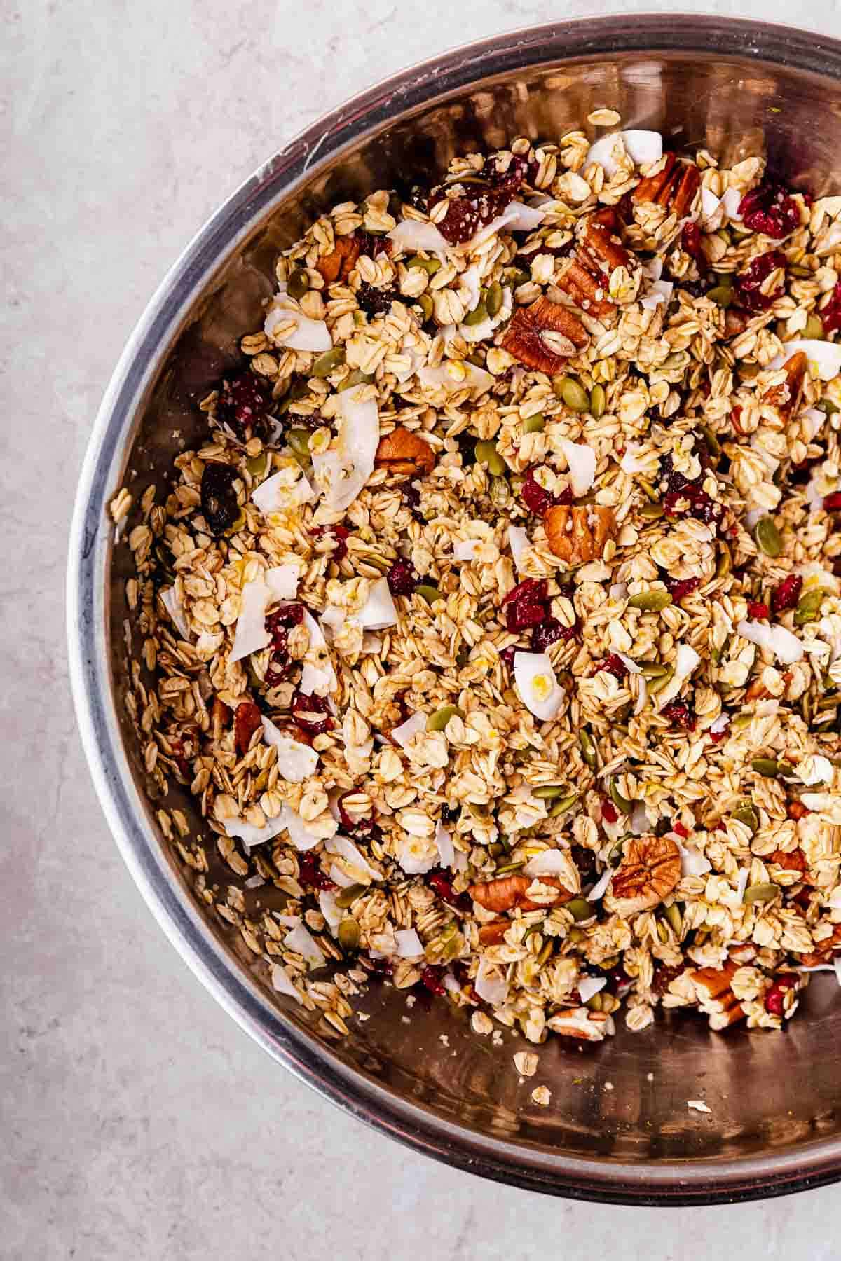 A large mixing bowl filled with raw oats and other ingredients to make orange pecan granola.