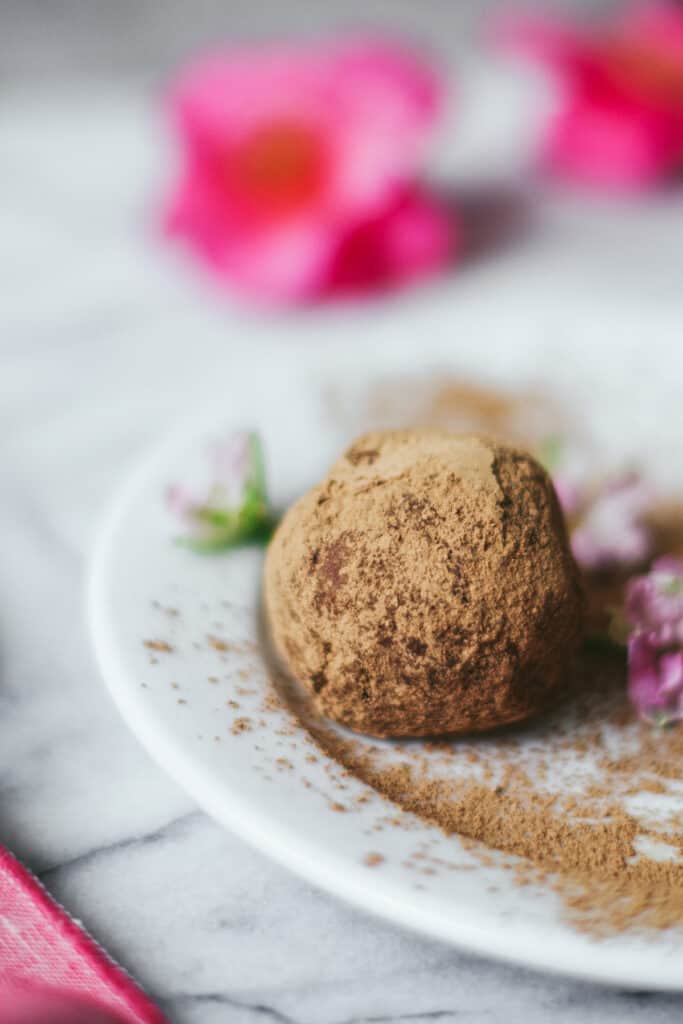 a close up of a rum ball on a white plate surrounded by pink flowers