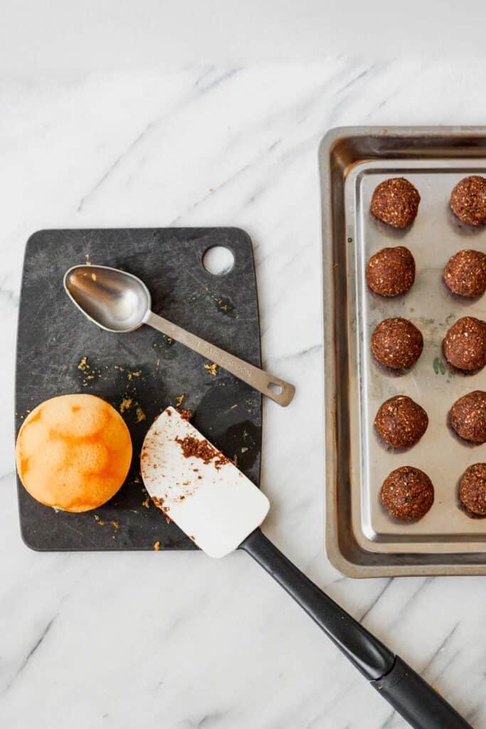 a zested orange and a chocolate dipped spoon next to a tray of bliss balls