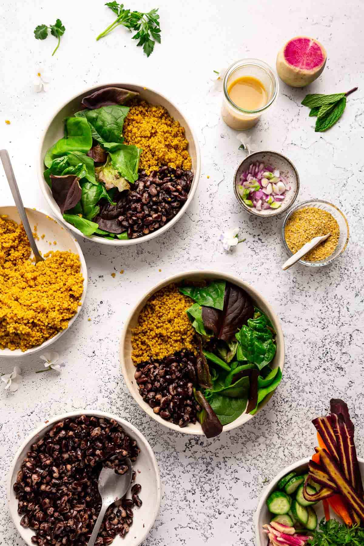 Greens, beans, and quinoa in serving bowls surrounded by other ingredients.