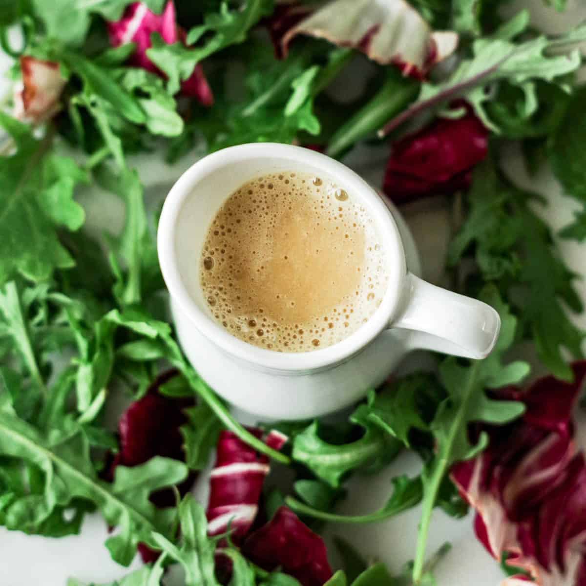 Lemon oil-free salad dressing in a small pitcher surrounded by greens.