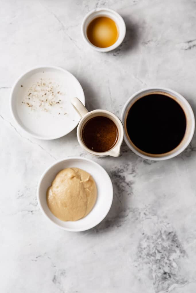 tahini balsamic salad dressing in a small pitcher surrounded by its ingredients