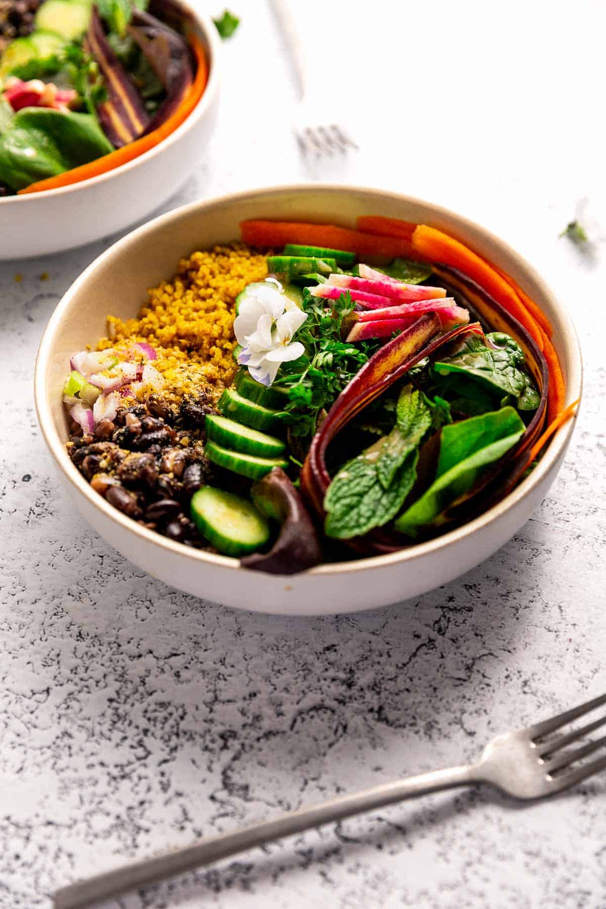 A rainbow-colored bowl of veggies, beans, and quinoa with a flower on top.