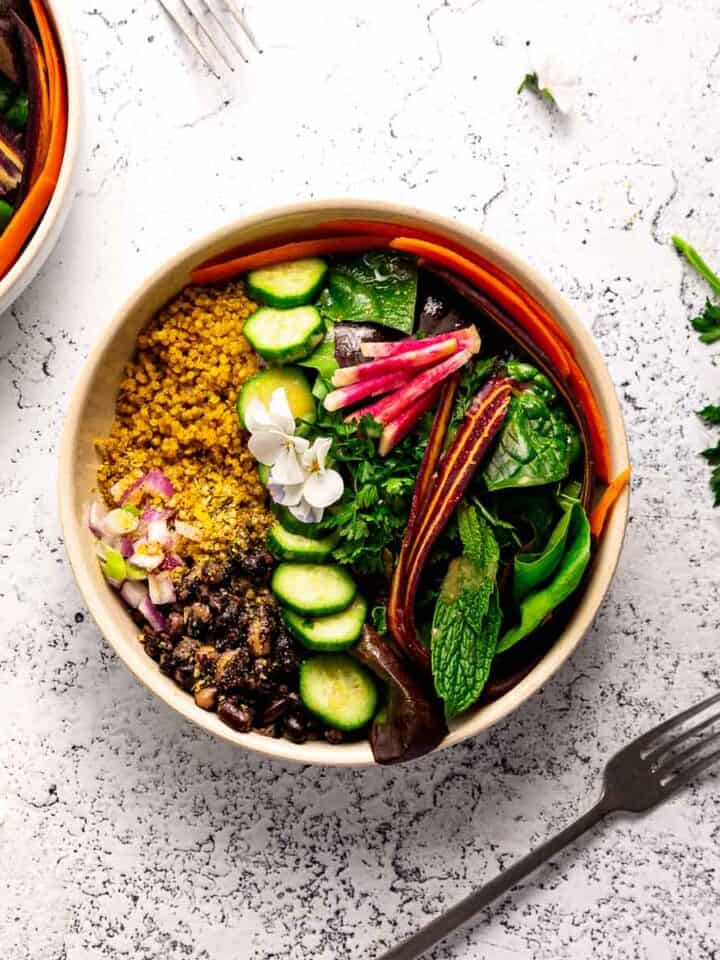 A bowl full of colorful veggies, golden curry quinoa, and black beans.
