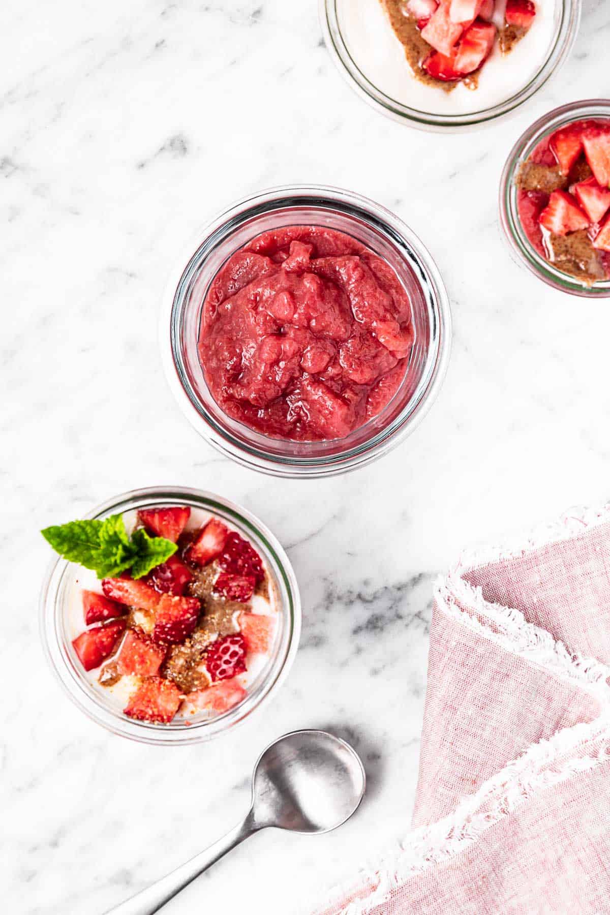 A jar of rhubarb ginger compote surrounded by parfaits topped with strawberries and mint.