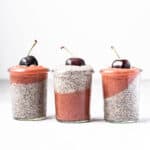 Three jars of white chia pudding and rhubarb ginger compote, with a fresh cherry on top of each.