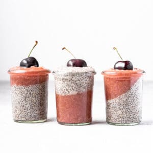 Three jars of white chia pudding and rhubarb ginger compote, with a fresh cherry on top of each.