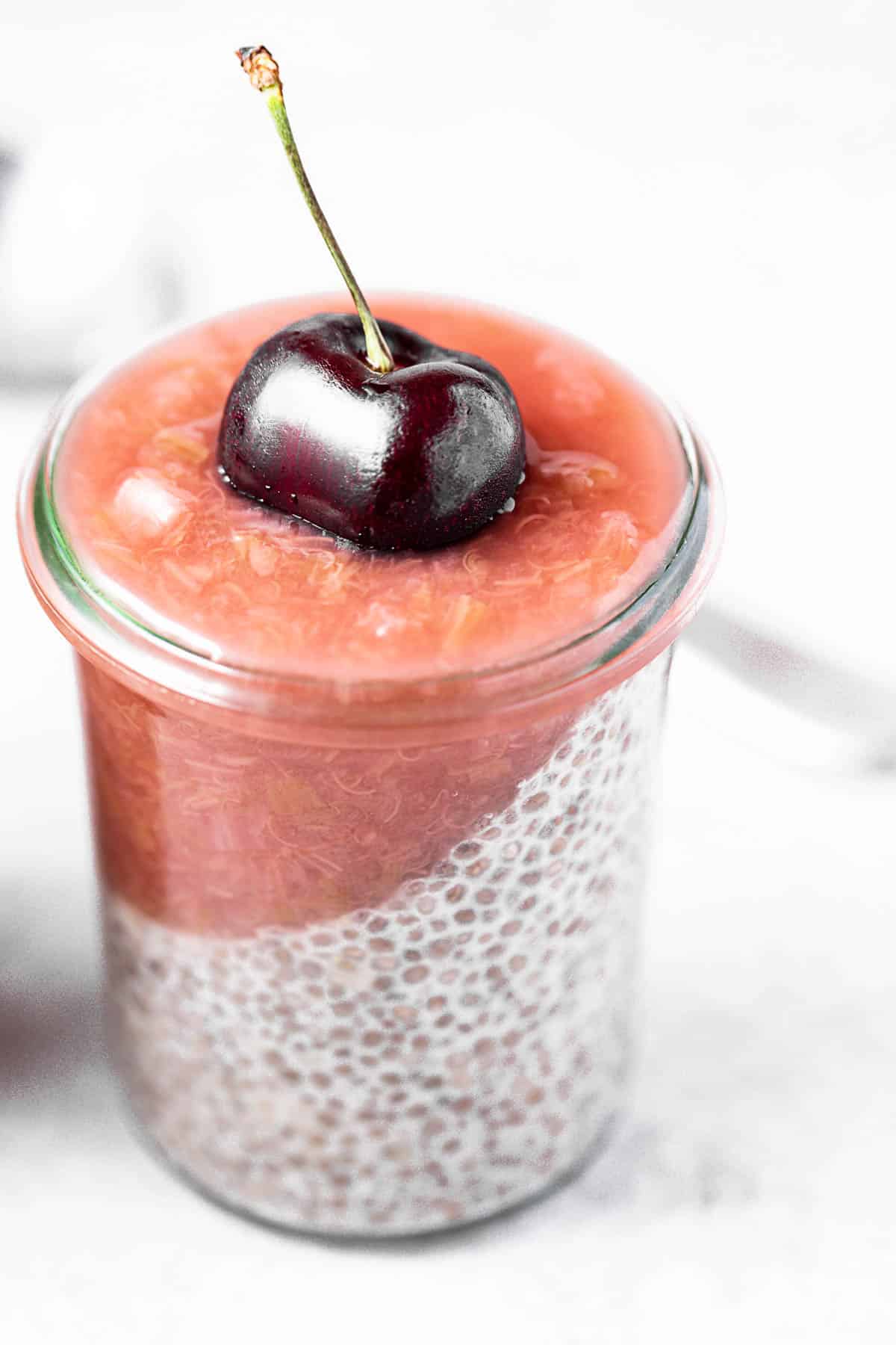 A closeup view of a chia pudding parfait topped with rhubarb ginger compote and a cherry.