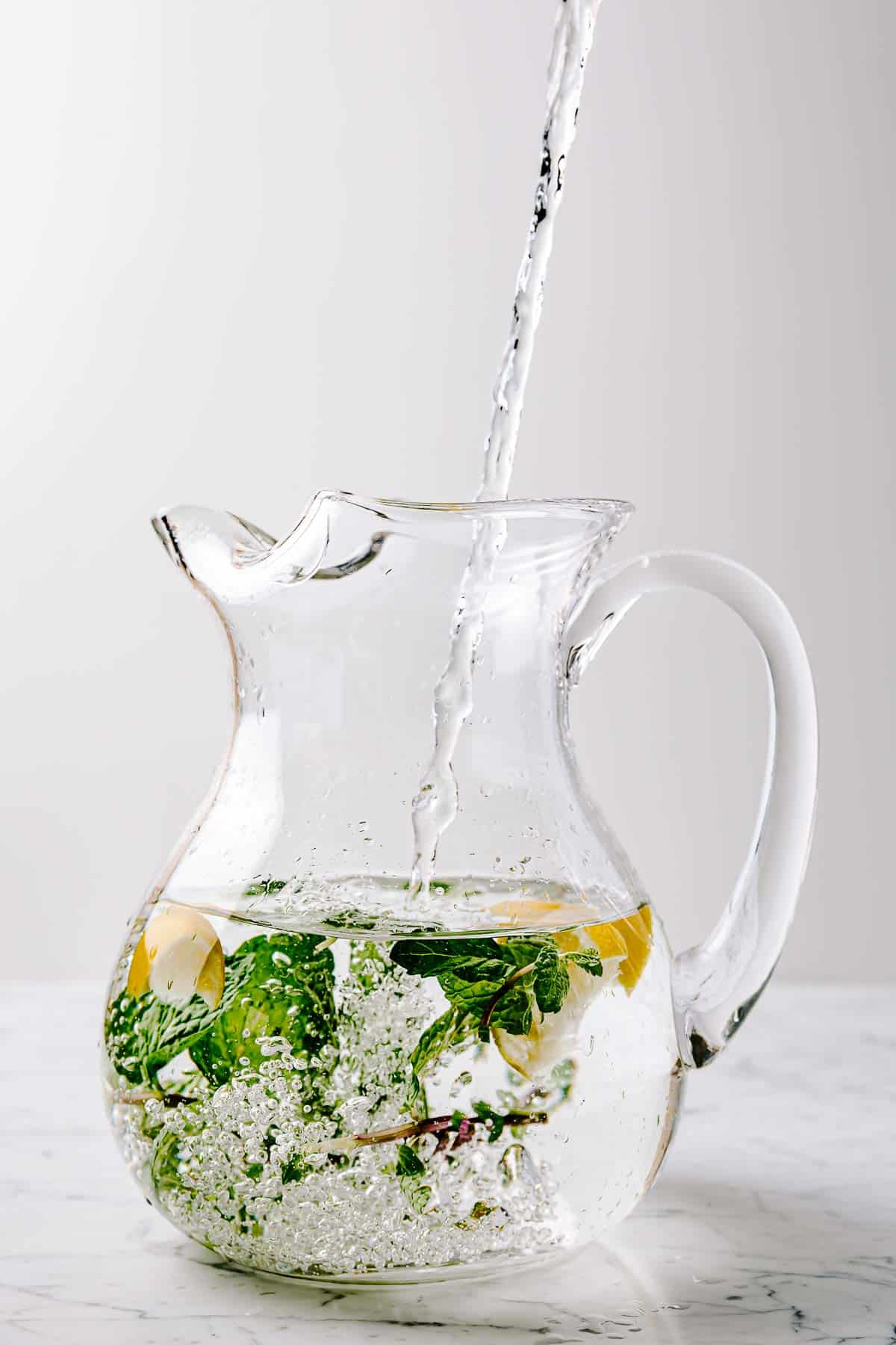Lemon and mint in a glass pitcher filling with water.