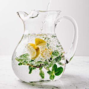 A glass pitcher of lemon mint water on a marble surface.