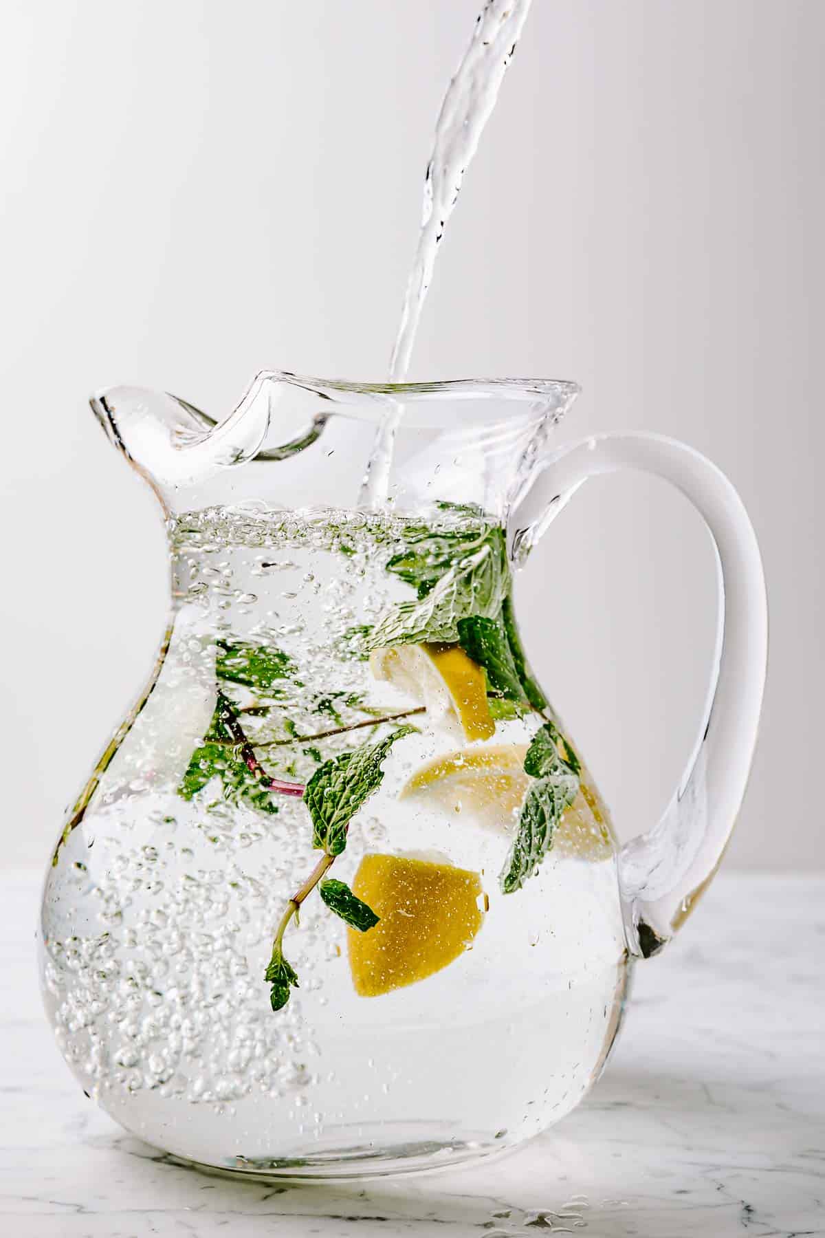 A glass pitcher filled with water and a few lemon wedges and mint sprigs.