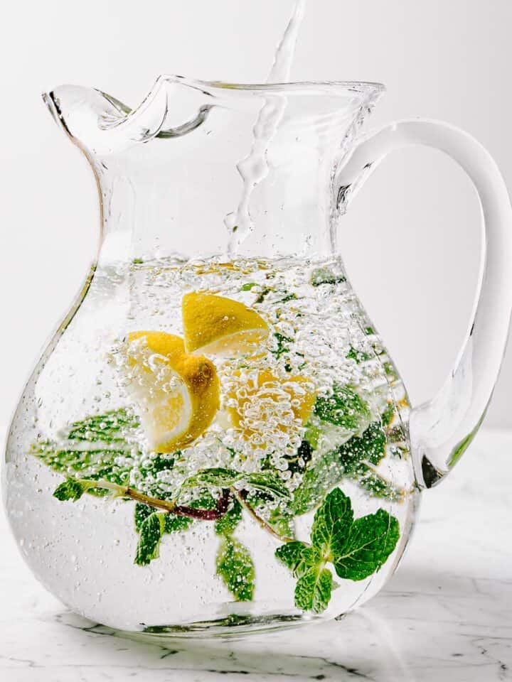 A glass pitcher of lemon mint water on a marble surface.