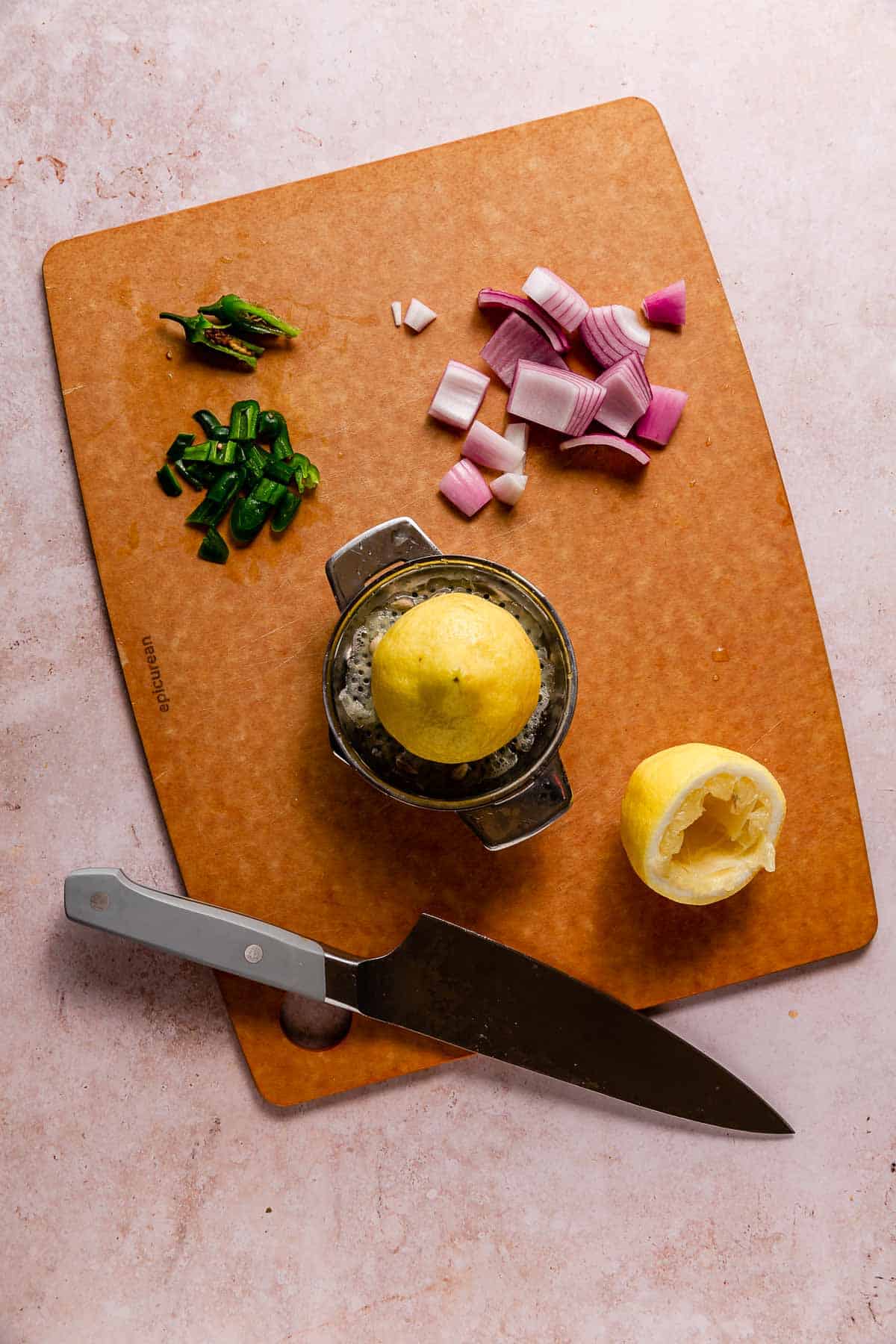 A lemon being juiced next to chopped jalapeno and red onion on a cutting board.