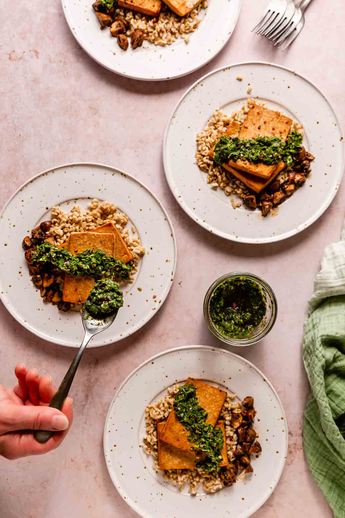 A hand spooning chimichurri onto tofu steaks.