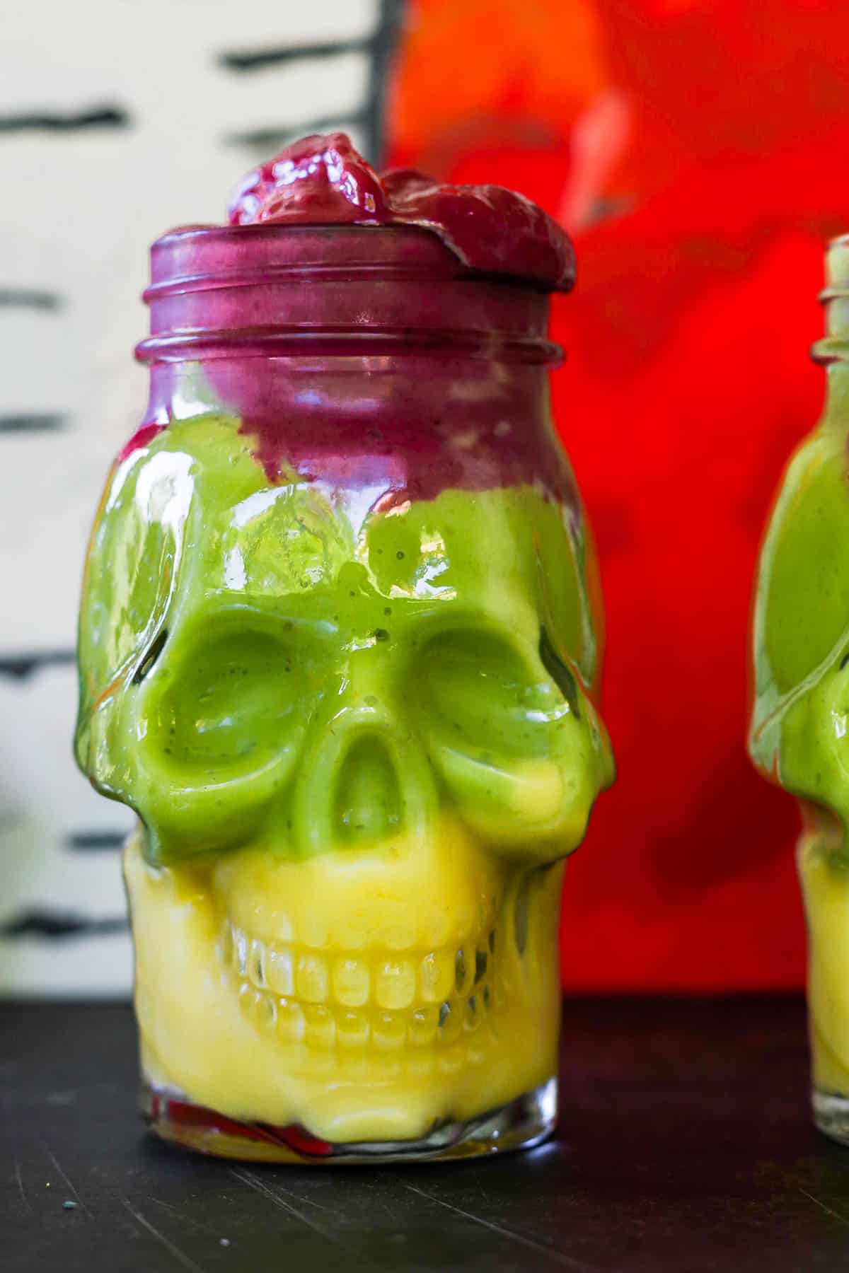 Yellow, green, and purple smoothies stacked in a skull-shaped jar.