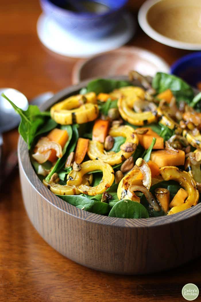 A serving bowl of salad with delicata squash and persimmon pieces on top of the greens.