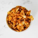 Vegan coconut bacon in a small bowl on a marble surface.