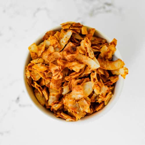 Vegan coconut bacon in a small bowl on a marble surface.