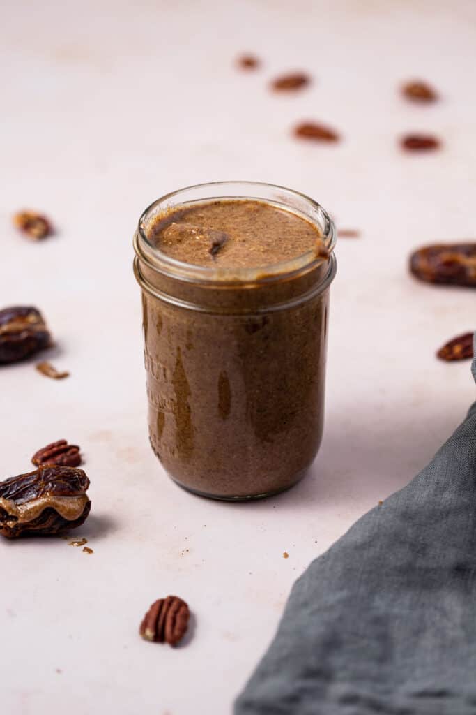 a jar of pecan butter surrounded by pecans and dates