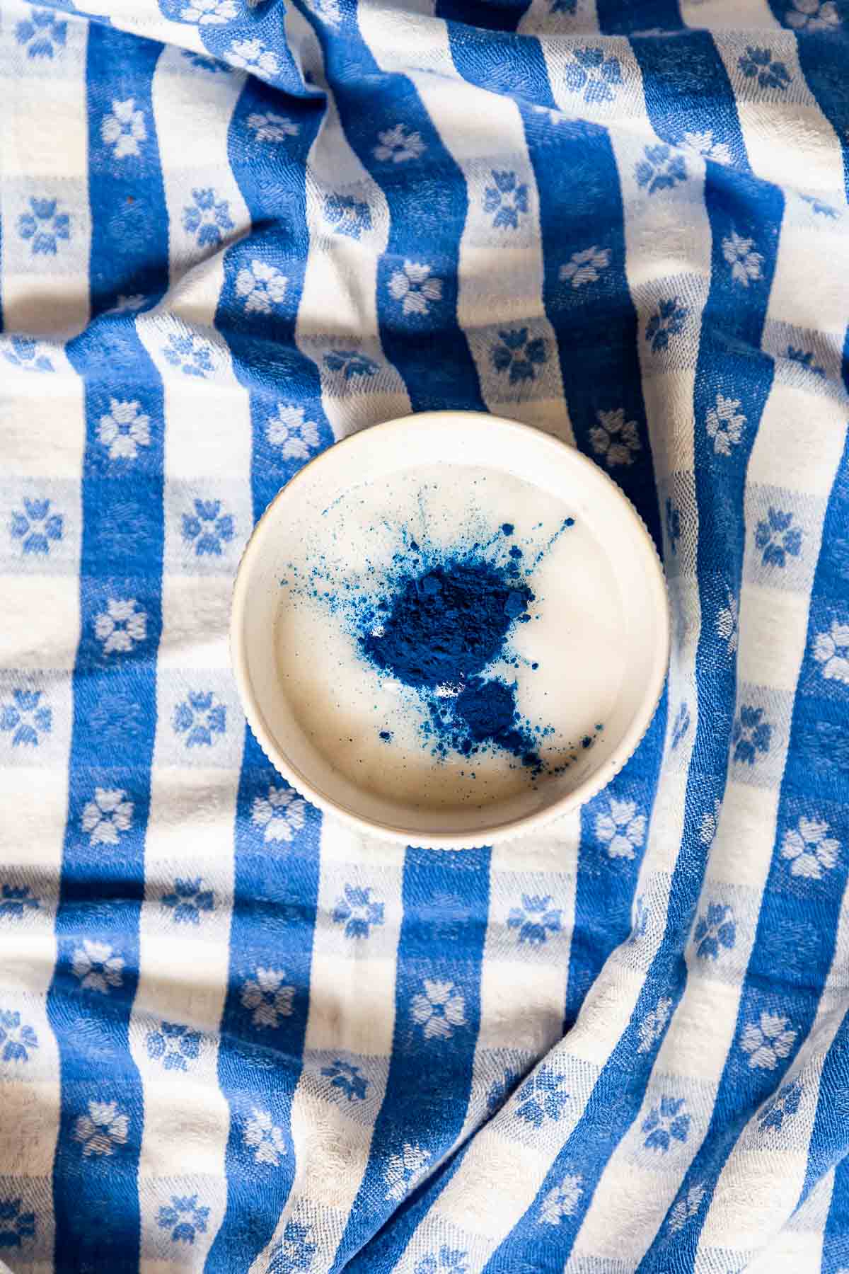 Natural blue powder on top of white yogurt in a ramekin on a blue gingham tablecloth.