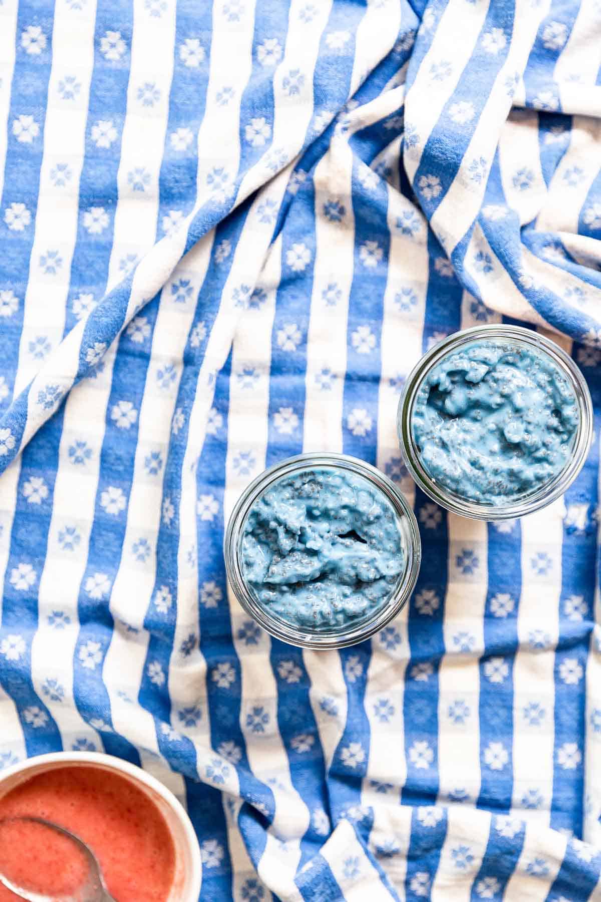 Blue chia yogurt in a glass jar on top of a blue gingham tablecloth.