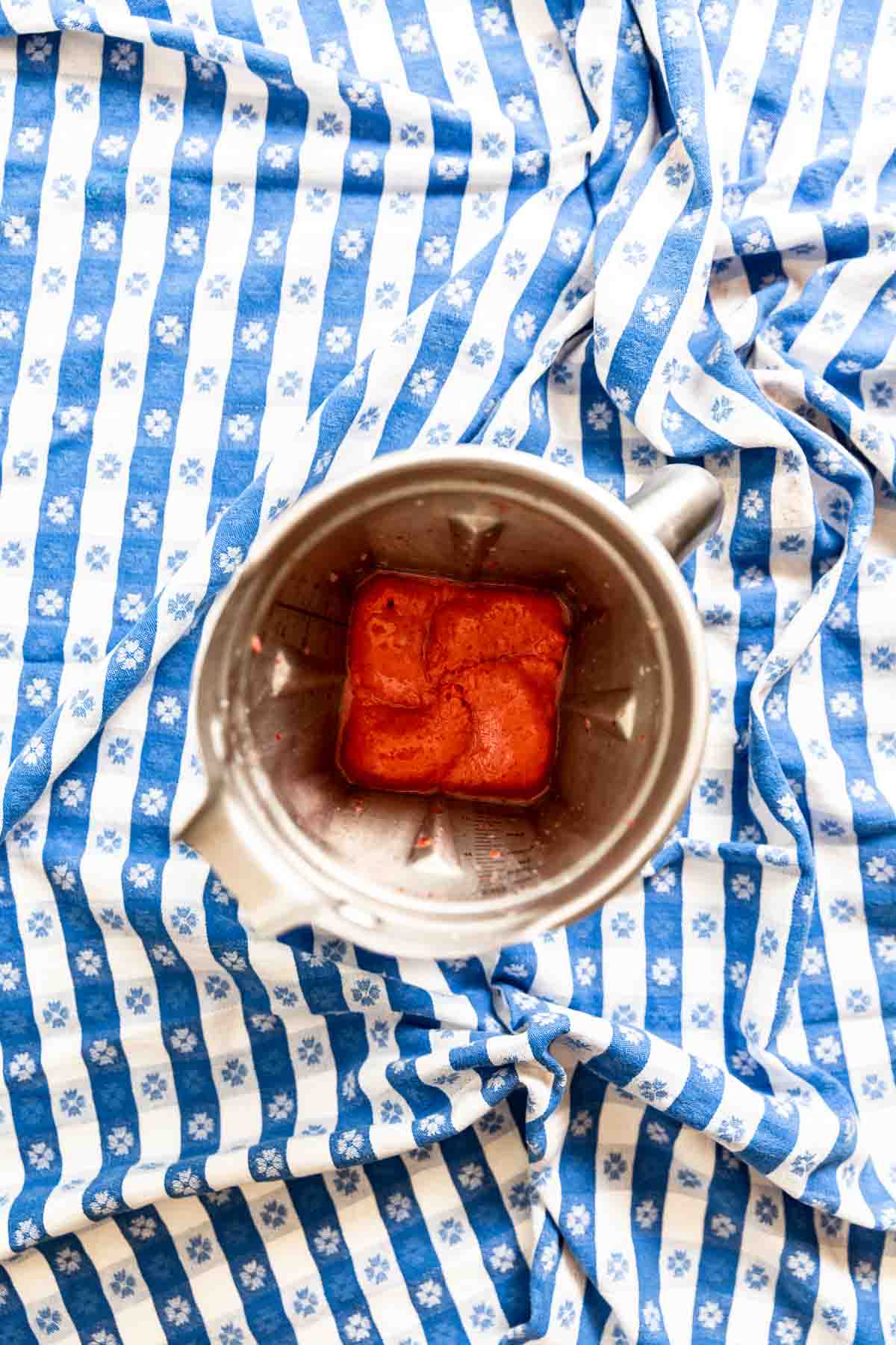 A stainless steel blender on a blue gingham tablecloth filled with strawberry smoothie.