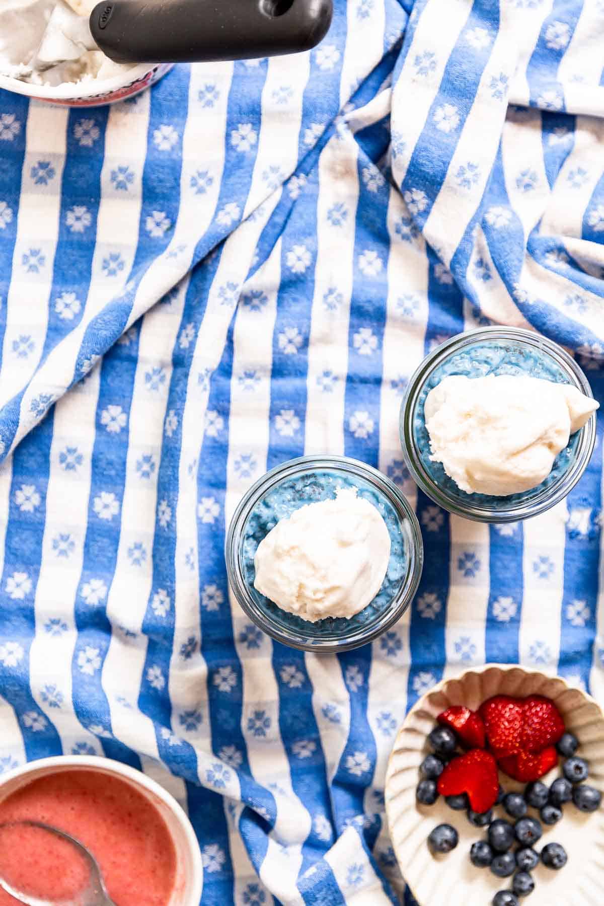 Whipped cream on top of blue chia yogurt on a blue gingham tablecloth.