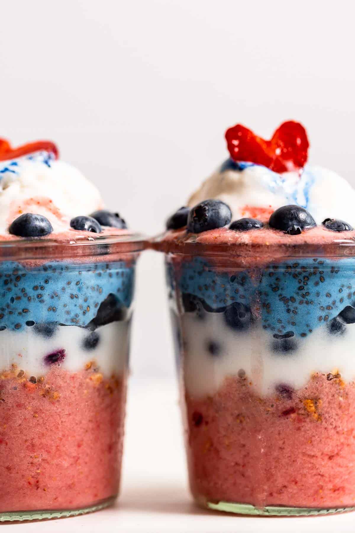 A closeup of two red, white, and blue dairy-free yogurt parfaits with strawberries on top.