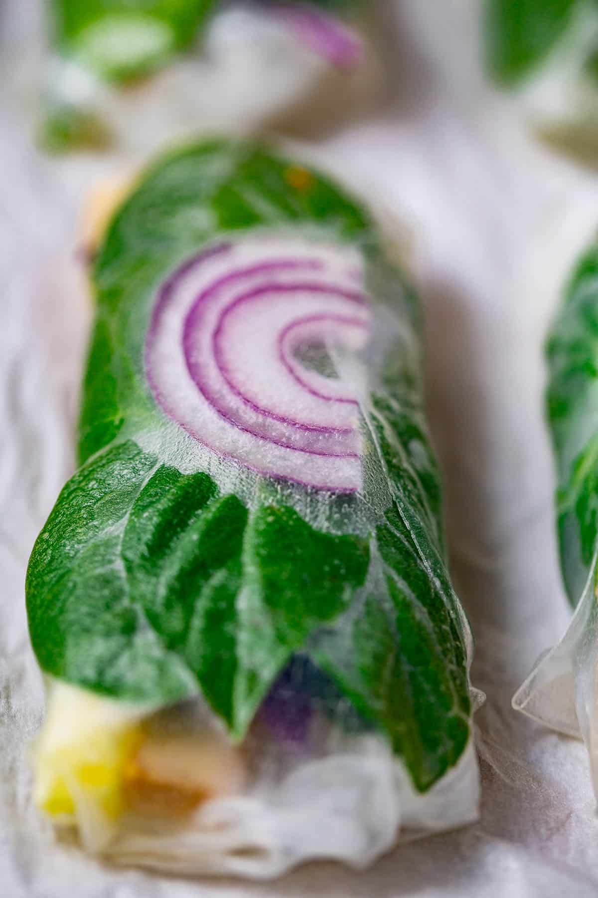 A closeup of one green and purple summer roll on white parchment.