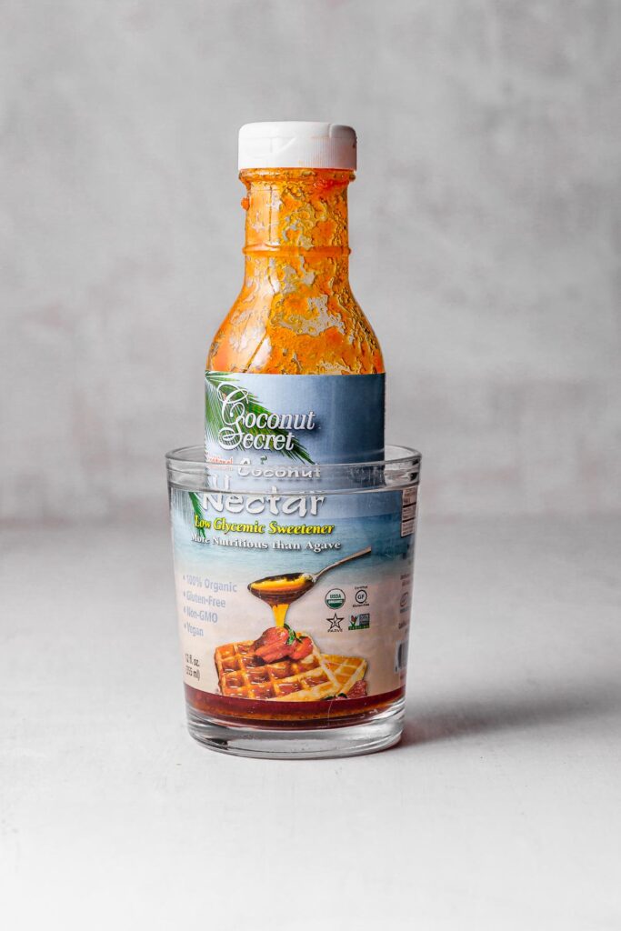 A bottle of coconut nectar sitting in a glass of warm water to soften.