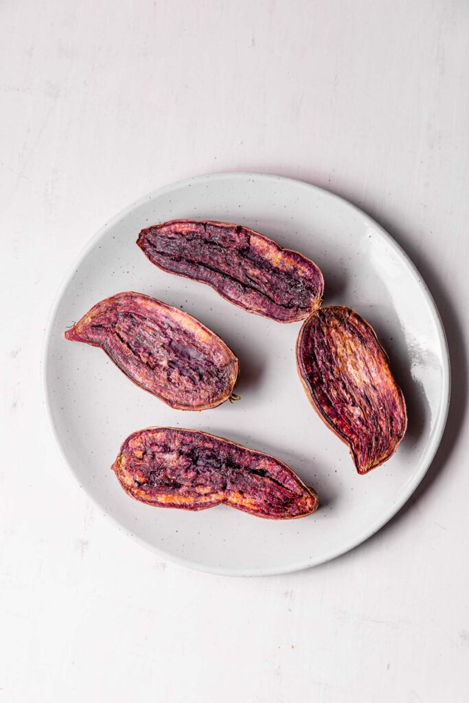 Four slices of purple roasted sweet potatoes on a plate.