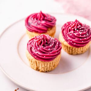 Vibrant pink frosting swirled on top of three cupcakes on a plate.