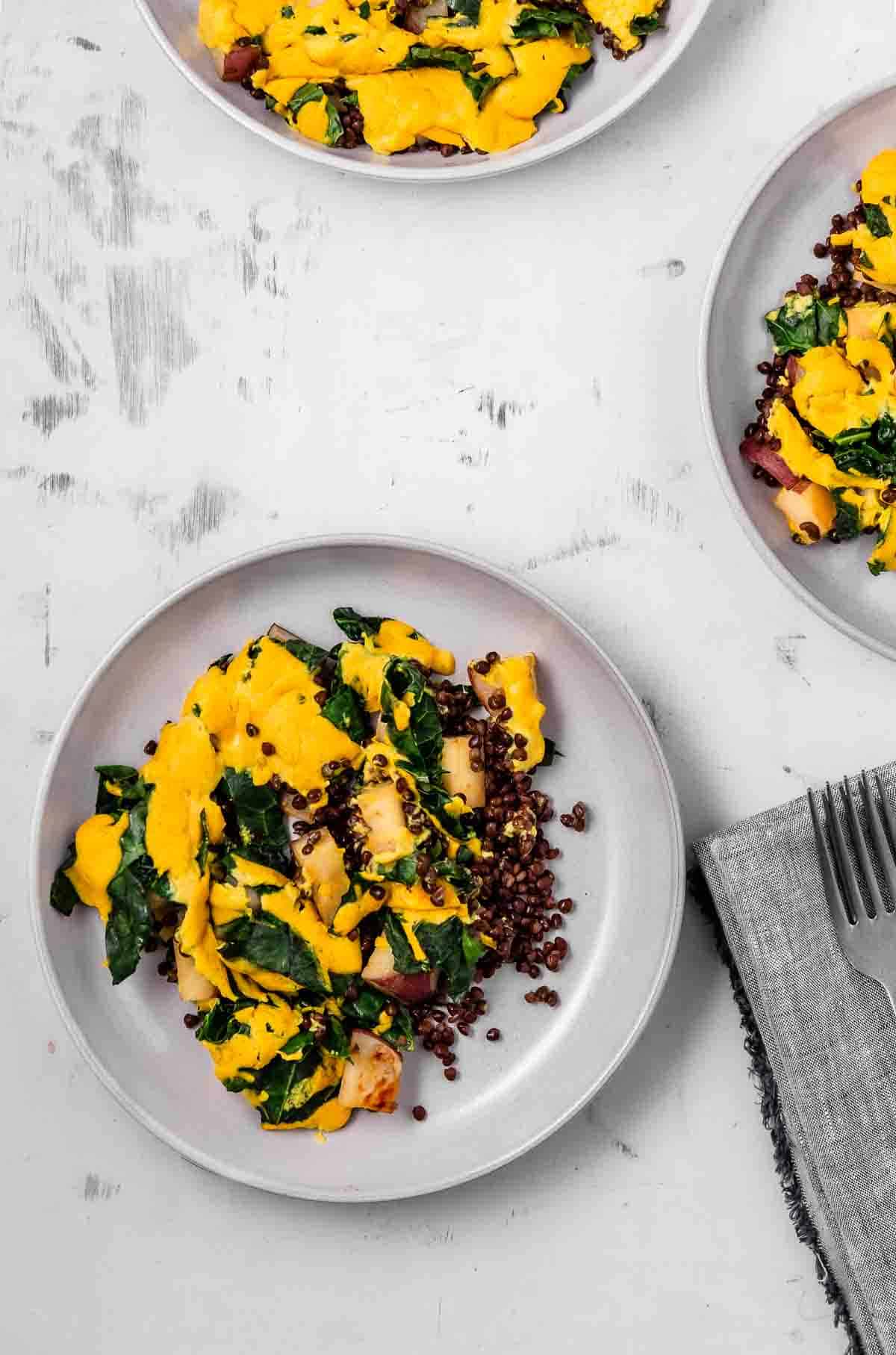 A grey plate of cheesy roasted potatoes with greens and lentils.